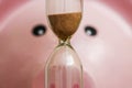 Close-up of a pink porcelain piggy bank looking at the hourglass. Concept of saving money and passing time