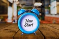 New Start text on Alarm Clock on wooden table.