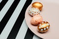 Close up of pink, white and golden decorated eeaster eggs on pink plate on striped background. Trendy holiday background