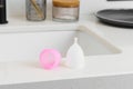 Close-up of a pink and white menstrual cup on the edge of a bathroom sink. Concept of care during menstruation and reusable