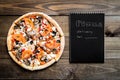 Close-up of pizza and notebook with the text: Pizza delivery. background wooden table. Notebook black with white text Royalty Free Stock Photo