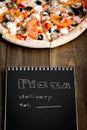 Close-up of pizza and notebook with the text: Pizza delivery. background wooden table. Notebook black with white text Royalty Free Stock Photo