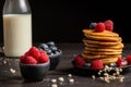 Close-up of plate with stacked pancakes, blueberries, raspberries and bottle of milk, on table and dark background Royalty Free Stock Photo