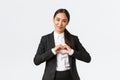 Close-up of pleasant asian businesswoman, saleswoman in black suit care for her clients, showing heart sign and smiling