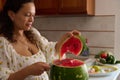 Close-up of a pleasant housewife cutting ripe organic juicy watermelon in the rustic home kitchen interior