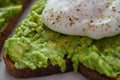 Close up of a poached egg on a smashed avocado toast with ground black pepper.