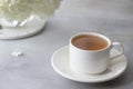 Close-up of a porcelain cup with herbal tea on a blurry background of white flowers.