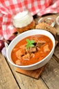 Close-up of pork goulash with pieces of meat in a bowl, garlic, pepper, onion, glass with cold beer and red checkered