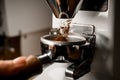 Close-up of portafilter in hands of barista into which coffee grinder pours ground coffee