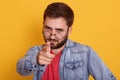 Close up portait of young caucasian man dresses red t sirt and denim jacket, pointing at camera, chhosing something, bearded guy Royalty Free Stock Photo