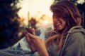 Close up portarit shot of beautiful joyful young woman using smartphone, enjoying her time outdoors, sitting in cozy chair
