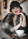 Close-up portrain of pretty woman wearing a hat Cloche sitting at a table in a coffee room and drinking coffee drink