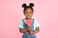 Close up portrait of adorable little African American black girl with red lollipop in heart shape isolated over pink Royalty Free Stock Photo