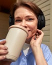 Close-up portrait of adorable mature woman with wireless headphones drinking coffee in outdoor cafe. Middle-aged smiling Royalty Free Stock Photo