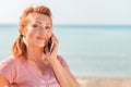 Close up portrait of an adult beautiful woman calling on the phone. In the background, the sea and a sandy beach. Copy space. Royalty Free Stock Photo