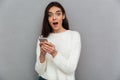 Close-up portrait of amazed woman in fluffy sweater holding smar