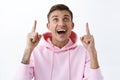 Close-up portrait of amused, rejoicing handsome blond guy in pink hoodie, look up with joyful amazed smile, looking at