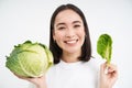 Close up portrait of asian woman, biting lettuce, eating green cabbage and smiling, white background Royalty Free Stock Photo