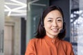 Close up portrait of Asian woman inside modern office with headset for video call, woman smiling and looking at camera Royalty Free Stock Photo