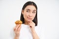 Close up portrait of asian woman with pensive smiling face, holding cupcake, thinking of bakery pastry, white background