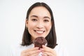 Close up portrait of asian woman smiles, eats chocolate cupcake with pleased face, isolated on white background Royalty Free Stock Photo