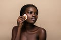 Close up portrait of an attractive african american woman removing makeup with sponge isolated on beige background Royalty Free Stock Photo