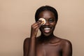 Close up portrait of an attractive african american woman removing makeup with sponge isolated on beige background Royalty Free Stock Photo