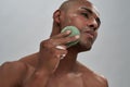 Close up portrait of attractive african american young man enjoying skincare procedure, using cleansing sponge while Royalty Free Stock Photo