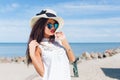 Close-up portrait of attractive brunette girl with long hair standing on the beach near sea. She wears hat, sunglasses Royalty Free Stock Photo