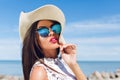 Close-up portrait of attractive brunette girl with long hair standing on the beach near sea. She wears hat, sunglasses Royalty Free Stock Photo