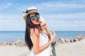 Close-up portrait of attractive brunette girl with long hair standing on the beach near sea. She wears hat, sunglasses Royalty Free Stock Photo