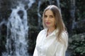 Close up portrait of attractive Caucasian woman near waterfall. Female with long blond hair wearing white dress. Water splash. Royalty Free Stock Photo