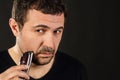 Close up portrait of an attractive Eatsern European man trimming his beard. Black background with copy space Royalty Free Stock Photo