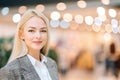 Close-up portrait of attractive elegance young blonde woman looking at camera standing in hall of mall centre, blurred Royalty Free Stock Photo