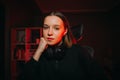 Close-up portrait of an attractive female gamer in a headset around her neck sitting at night in a bedroom with a red light and