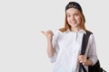 Close up portrait of attractive female student wearing cap, white blouse and backpack, pointing aside with her thumb, isolated on Royalty Free Stock Photo