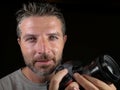 Portrait of attractive and handsome man on his 30d holding professional reflex photo camera next to his face smiling happy Royalty Free Stock Photo
