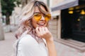 Close-up portrait of attractive joyful girl with amazing smile wears stylish yellow sunglasses and white shirt. Stunning