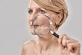 Close up portrait of attractive middle aged woman looking aside, holding a magnifying glass and showing her wrinkles Royalty Free Stock Photo