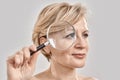 Close up portrait of attractive middle aged woman looking aside, holding a magnifying glass and showing her wrinkles Royalty Free Stock Photo