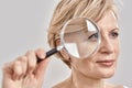 Close up portrait of attractive middle aged woman looking aside, holding a magnifying glass and showing her wrinkles Royalty Free Stock Photo