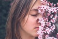Close up portrait of attractive romantic teenage girl smelling aroma of blooming spring pink plum tree flowers with closed eyes. Royalty Free Stock Photo