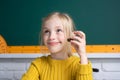 Close-up portrait of attractive small little cheerful girl sitting on table desktop in class room, chocolate. Little