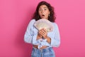 Close up portrait of attractive woman holding fan of money in her hands, keeps mouth opened, wearing stylish clothng, wins lottery Royalty Free Stock Photo