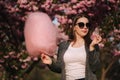 Close up portrait of attractive young girl eating cotton candy in front of pink sakura tree Royalty Free Stock Photo