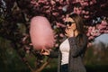 Close up portrait of attractive young girl eating cotton candy in front of pink sakura tree Royalty Free Stock Photo