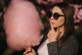 Close up portrait of attractive young girl eating cotton candy in front of pink sakura tree Royalty Free Stock Photo