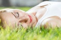 Close up portrait of an attractive young woman laying down on green grass in a park during the summer and listening to Royalty Free Stock Photo