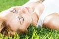 Close up portrait of an attractive young woman laying down on green grass in a park during the summer and listening to Royalty Free Stock Photo