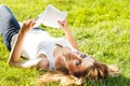 Close up portrait of an attractive young woman laying down on green grass in a park during the summer and listening to Royalty Free Stock Photo